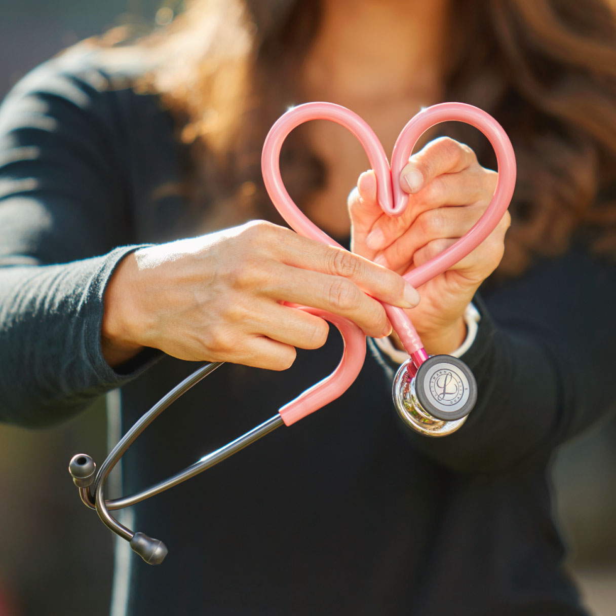 pink stethoscope in shape of heart held by a woman