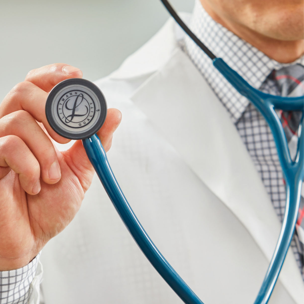 doctor in white coat holds up head of stethoscope to display Littmann logo