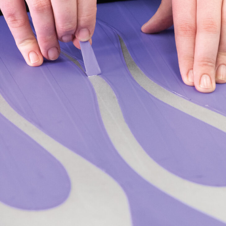hands pulling out cut areas of tape of paint stencil