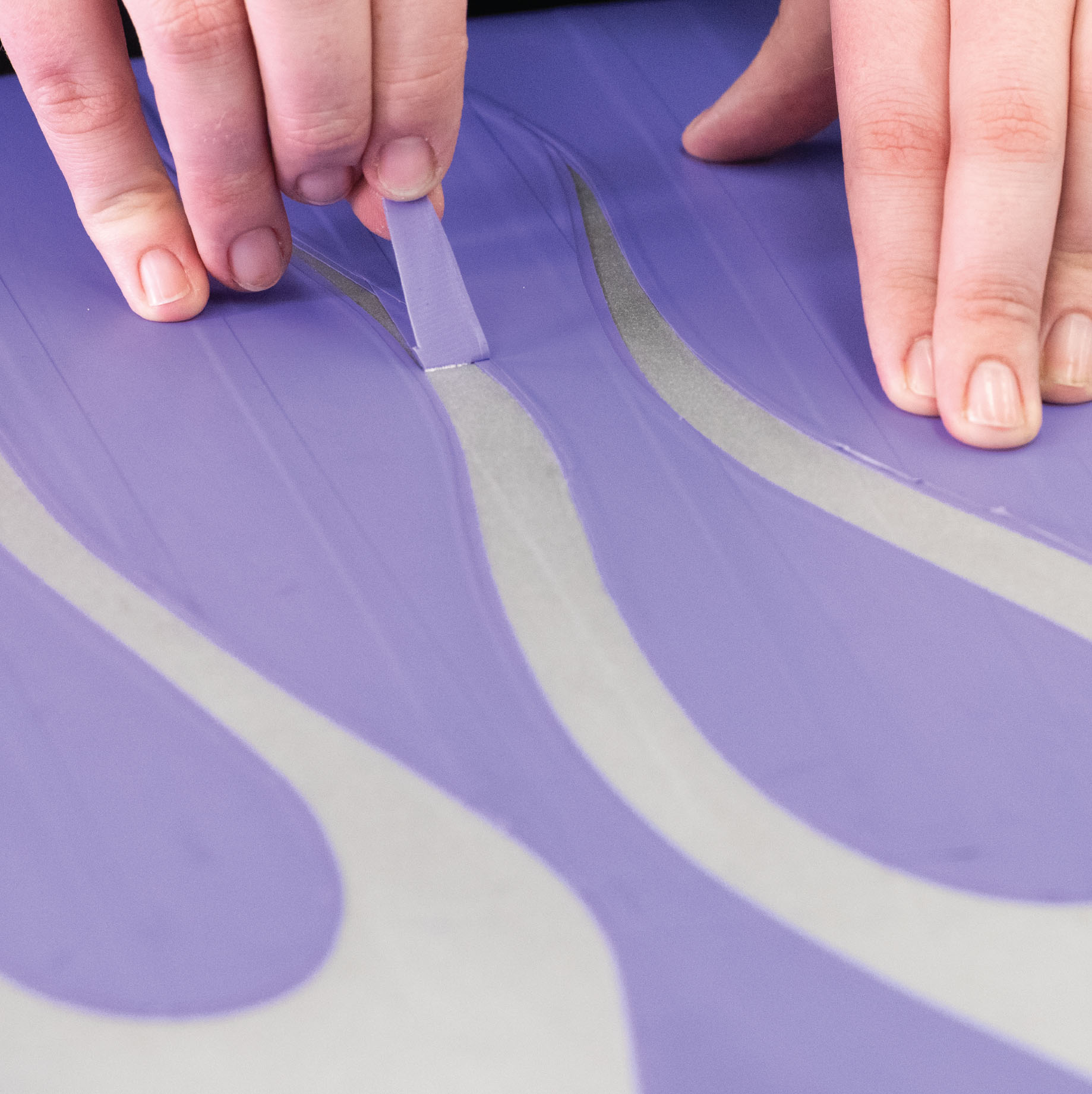 hands pulling out cut areas of tape of paint stencil
