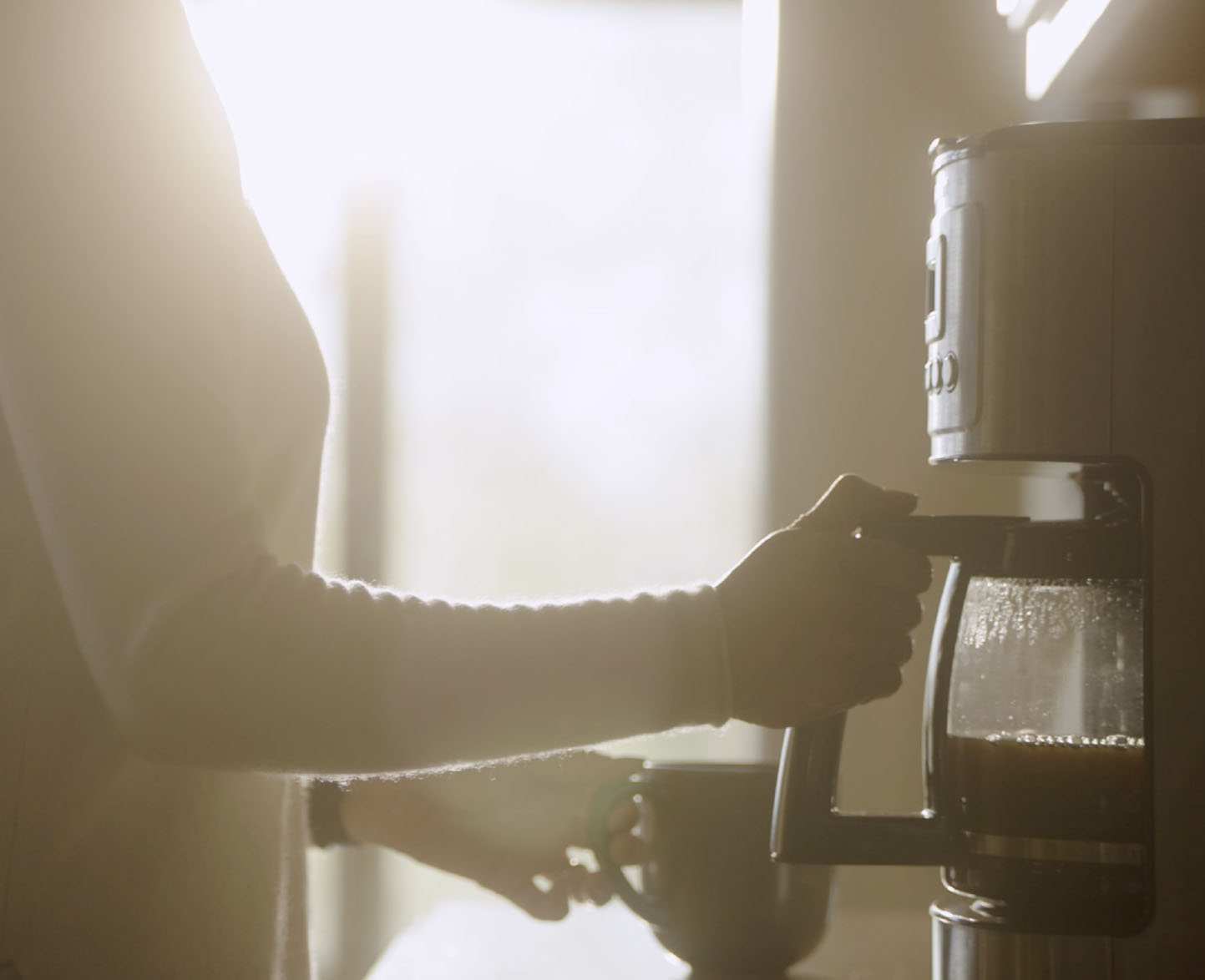 female person pulls coffee pot from drip coffee machine