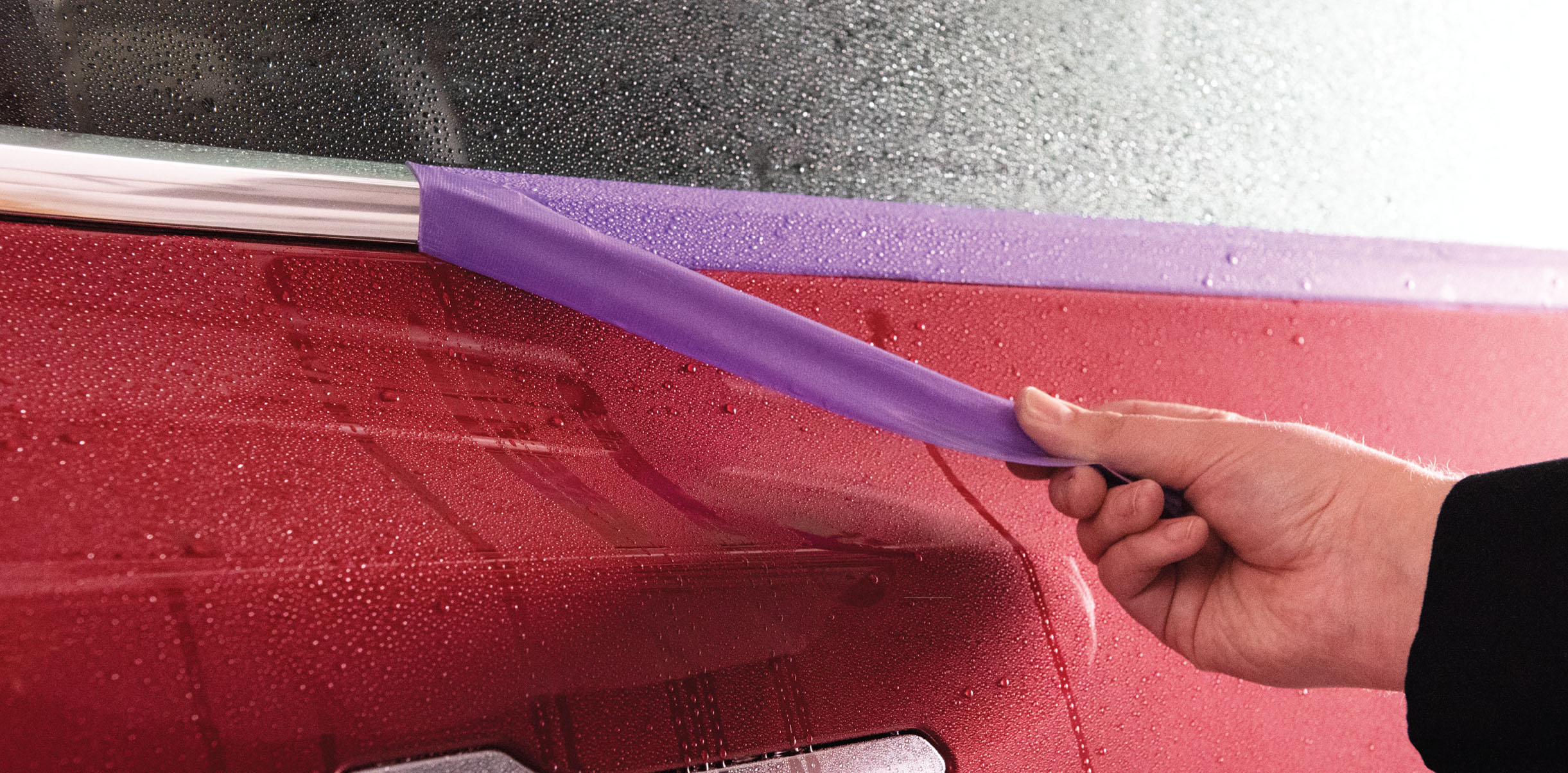purple precision poly tape being removed from chrome trim of red vehicle